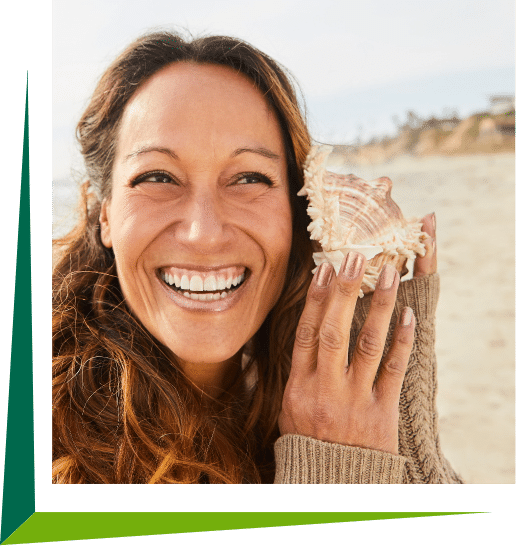 Woman at the beach holding a sea shell to her ear